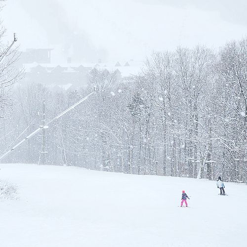 Father and child ski in fluffy snowflakes near the base of the mountain