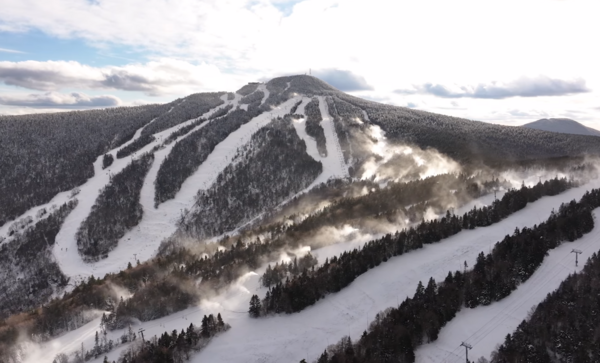 Snow-covered ski trails on a mountain with snowmaking guns on some of the trails