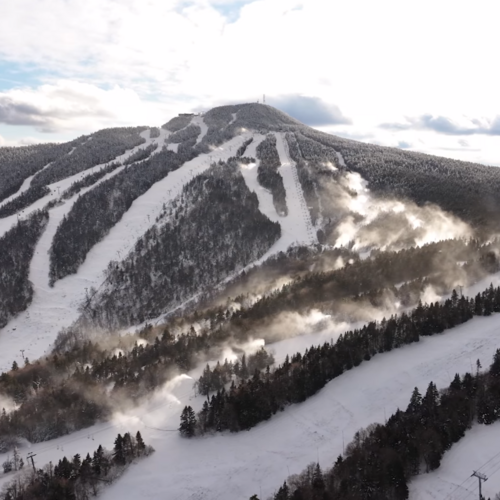 Snow-covered ski trails on a mountain with snowmaking guns on some of the trails